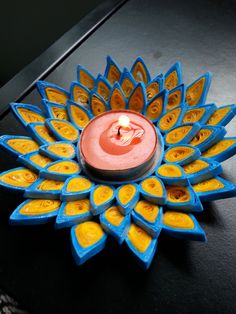 a blue and yellow candle sitting on top of a black table next to a flower