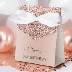 a pink and gold birthday gift bag with a white bow on it, surrounded by confetti and balloons