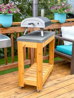 an outdoor grill on a wooden deck with potted flowers in the back and blue cushions