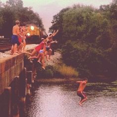 a group of people jumping into the water from a bridge