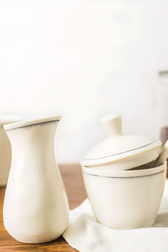 two white vases sitting next to each other on top of a wooden tablecloth