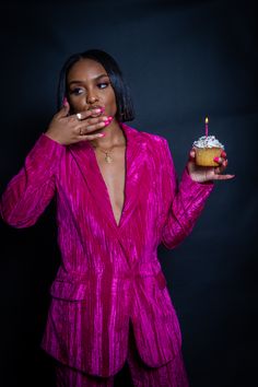 a woman in a pink suit holding a cupcake with a lit candle on it