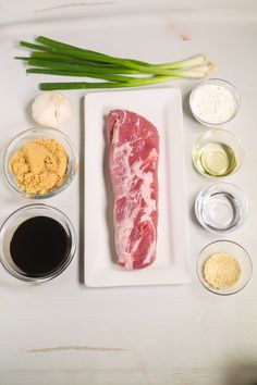 raw meat and ingredients laid out on a white plate with green onions, garlic, oil, seasonings, and spices