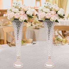 two silver vases with white flowers in them on top of a dining room table