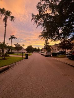 cars are parked on the street in front of palm trees and houses at sunset or dawn