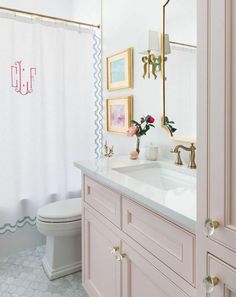 a bathroom with pink cabinets and gold accents on the mirror above the sink is a white toilet