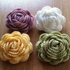 four crocheted flowers sitting on top of a wooden table