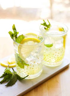 two glasses filled with lemonade and mint garnish on top of a tray