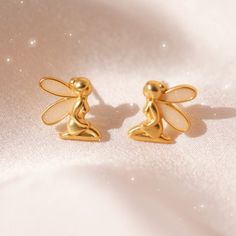 "Fairy Earrings - add a little magic with our adorable fairy stud earrings! Dainty matte gold stud earrings with shimmery fairy wings. Such a cute touch for your cottagecore or fairy dress fits! Wildflower + Co.Jewelry ♥ Measurements: dainty - a little under 1/2\"\" ♥ Materials: matte gold dipped metal & glitter enamel. Posts are titanium - good for sensitive ears! ♥ Packaged in our cute gift box ♥ Designed by & exclusive to Wildflower + Co. ♥ Imported ♥ Product safety - intended for use by adul Fairy Style Gold Jewelry For Gift, Fairycore Earrings For Pierced Ears As A Gift, Gold Fairycore Jewelry Gift, Gold Fairy Style Handmade Earrings, Gold Fairy Earrings For Gift, Cute Fairy Earrings, Gold Handmade Fairy Earrings, Handmade Gold Fairy Earrings, Fairy-themed Drop Earrings For Gifts