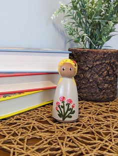 a wooden doll sitting next to a stack of books and a potted plant on a table