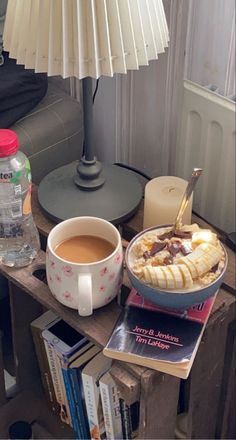 a table topped with a bowl of food and a cup of coffee next to a lamp