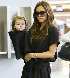 a woman carrying a baby in her arms at an airport with other people behind her