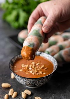 a person dipping some kind of sauce into a bowl with peanuts on the side and other vegetables in the background