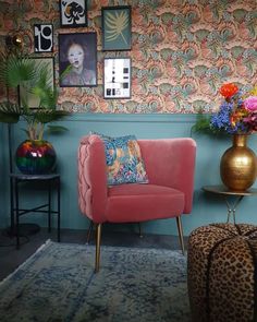 a pink chair sitting in front of a blue wall with pictures on it and a leopard print ottoman