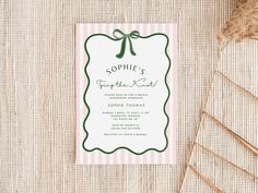 a pink and green striped wedding card with a bow on the front, sitting on top of a table