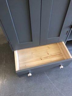 a wooden drawer in the middle of a gray kitchen cabinet with metal handles and knobs