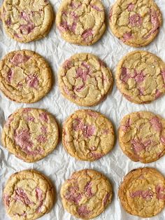 freshly baked cookies with pink icing on white parchment paper lined up in rows, top view