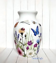 a white vase with colorful flowers and butterflies painted on the front, sitting on a wooden surface