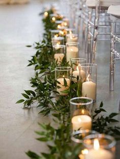 rows of candles are lined up on the floor next to each other with greenery