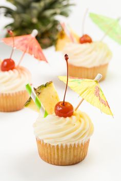 cupcakes with umbrellas and cherries on them sitting next to a pineapple