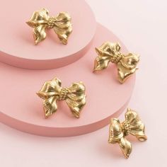 three pieces of gold colored metal with bows on pink plates next to eachother