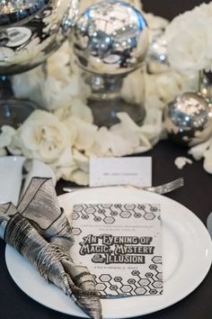 An Evening of Magic, Mystery, and Illusion place setting. A perfect theme for a end of year holiday gala, silver and black accents off set by white rose petals scattered across the table top with silver orbs. White Rose Petals, Place Settings Wedding