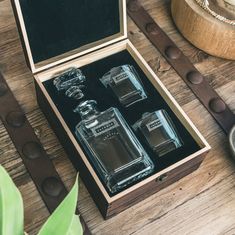 an open wooden box with two bottles in it sitting on a table next to a plant