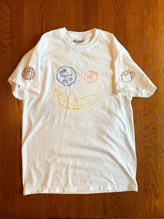 Brunch T-Shirt Hand drawn with fabric marker on white short sleeve unisex Gildan t-shirt, 100% cotton Features designs on front (blueberry yogurt, cutie, banana), left sleeve (stroopwafel), right sleeve (coffee cup) and back (artist's name) Small and Medium size available Note: Wash inside out on cold. Marker may fade a little after initial wash. No worries, it still looks great! Each shirt will either be shipped via bubble mailer or tube. Design by Josh Bokor Pre-shrunk Organic Cotton Short Sleeve Shirt, Unisex White T-shirt With Funny Print, White Short Sleeve T-shirt With Funny Print, Relaxed Fit Organic Cotton Tops With Custom Print, Organic Cotton Top With Custom Print In Relaxed Fit, Cotton Graphic Tee With Cartoon Print, Cotton Cartoon Print Graphic Tee, Fun Cotton T-shirt With Funny Print, Cute Short Sleeve T-shirt With Screen Print