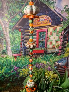 there is a tall pole made out of beads and other things in front of a painting