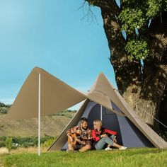 two people sitting in a tent under a large tree with an awning over them