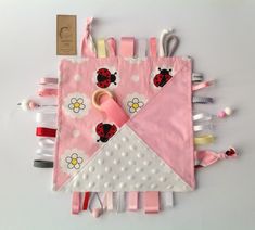 The sensory taggie blanket has ribbon tags, cords, teething rings and beads, plus a crinkle sound to occupy baby. Homemade Baby Toys, Baby Gifts To Make, Diy Tricot, Sensory Blanket