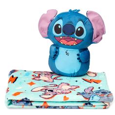 a blue stuffed animal sitting on top of a blanket next to two blankets with cartoon characters