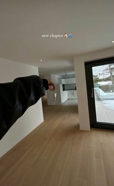 a man in black jacket standing on wooden floor next to sliding glass door and white wall