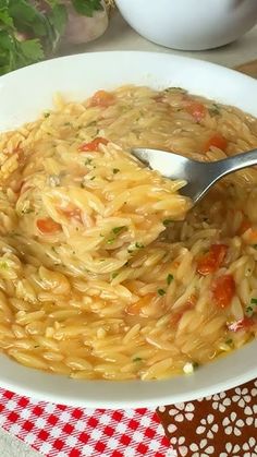 a white bowl filled with pasta on top of a red and white checkered table cloth