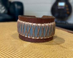 "One of a kind, upcycled leather bracelet made from used belts, upholstery scraps, and artistic findings. Every cuff is unique and made to wear and weather well.  Like high quality boots or your favorite leather journal, these cuffs get softer and more supple over time. The individual designs all start with the leather.  I use vintage belts, leather scraps, WW2 rifle holsters, and old horse bridles.  Each piece speaks to me, and informs the direction for the finished piece.  Adornments include found objects, printed leather, metal studs, gemstones, buttons - anything that will bring the cuff to life and make it a statement piece unlike any other. I prefer using a button & elastic closure when possible, as it makes the cuff fully adjustable.  It's a more labor and cost intensive process, bu Handmade Artisan Leather Bracelet, Rustic Leather Bracelet For Festivals, Adjustable Leather Cuff Bracelet Hand-stitched, Adjustable Hand-stitched Leather Cuff Bracelet, Unique Handmade Leather Cuff Bracelet, Unique Leather Cuff Bracelet With Strap, Rustic Handmade Leather Cuff Bracelet, Belts Leather, High Quality Boots