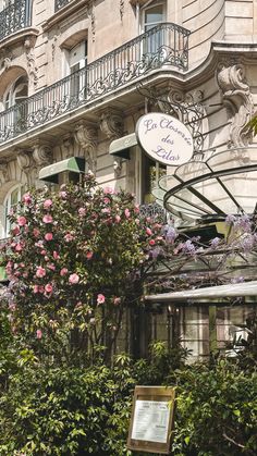 an old building with pink flowers in front of it and a sign on the outside