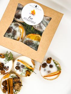 four decorated cupcakes in a box with pine cones on top and white frosting