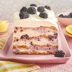 a piece of cake with white frosting and blackberries on top is sitting on a pink plate