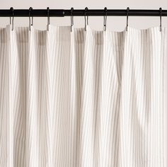 a white curtain hanging on a black rod with pinstripe pattern in the background