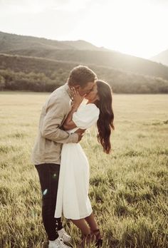 a man and woman kissing in the middle of a field with mountains in the background