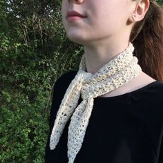 a woman wearing a white crocheted neck scarf in front of some green trees