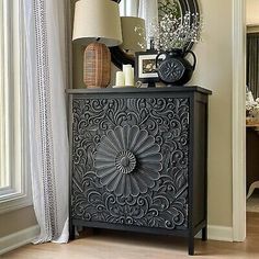 an ornate black cabinet with a mirror and vase on top in front of a window