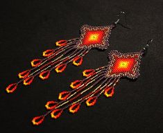 a pair of red and yellow beaded earrings on a black surface with an orange square in the center