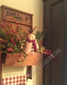 a snowman sitting on top of a wooden shelf next to a sign and flowers