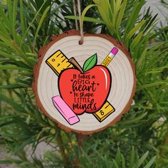 a wooden ornament with an apple and pencils on it hanging from a tree