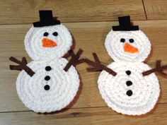 two crocheted snowmen sitting on top of a wooden floor