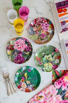 colorful plates and utensils laid out on a marble counter top with flowers painted on them