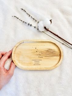 a person is holding a wooden tray with cotton on it and some dried flowers in the background