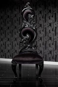 a black chair sitting in front of a wallpapered room with an ornate design on it