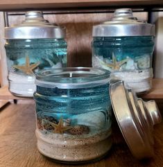 three jars filled with sand and starfish sitting on top of a wooden table next to each other